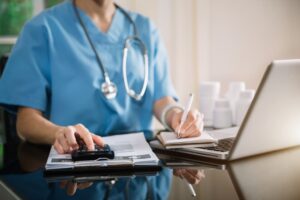 Hospital staff member calculating expenses and income using a calculator and writing notes, representing financial management in healthcare.