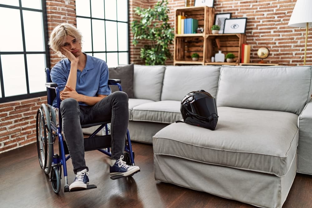 Joven en silla de ruedas reflexionando sobre un accidente de moto, parece fatigado y aburrido, mirando hacia la depresión, con los brazos cruzados en contemplación.