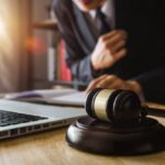 Legal proceedings: A male judge in a courtroom, using a gavel and digital tablet on a wooden table in the morning light.
