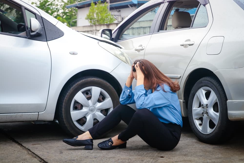 "Woman stressed after a car accident, having collided with another vehicle on a slippery, rain-slicked road.