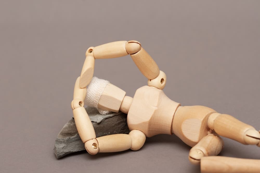 A wooden mannequin lying on a rock with a bandaged head, representing a head injury.