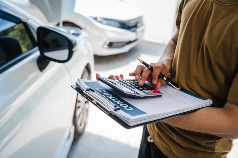 Man completing a car insurance form and discussing coverage with an adjuster after a car accident