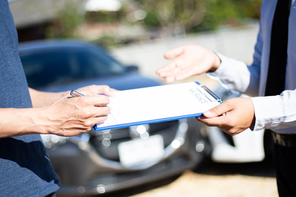 Customers and insurance agents sign documents to claim compensation after a car crash, highlighting the insurance process.