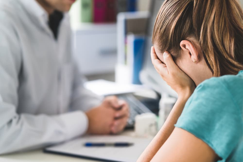 Doctor comforting distressed young woman, providing support for anxiety or mental health issues. Patient receiving medical guidance and emotional care.