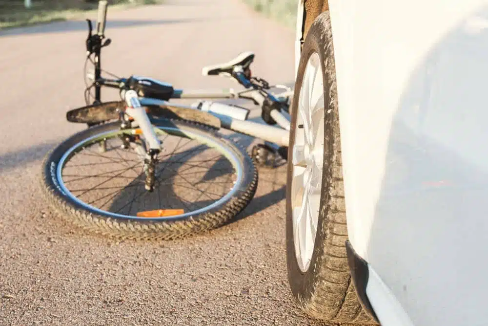 Primer plano de una bicicleta atrapada bajo las ruedas de un coche, que representa la escena de un accidente de tráfico y la seguridad vial.