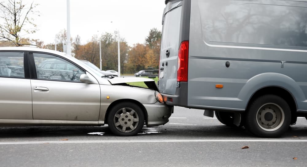 A gray sedan rear-ended a silver van on a road, causing visible front-end damage to the sedan and minor marks on the van. Trees and streetlights are visible in the background.