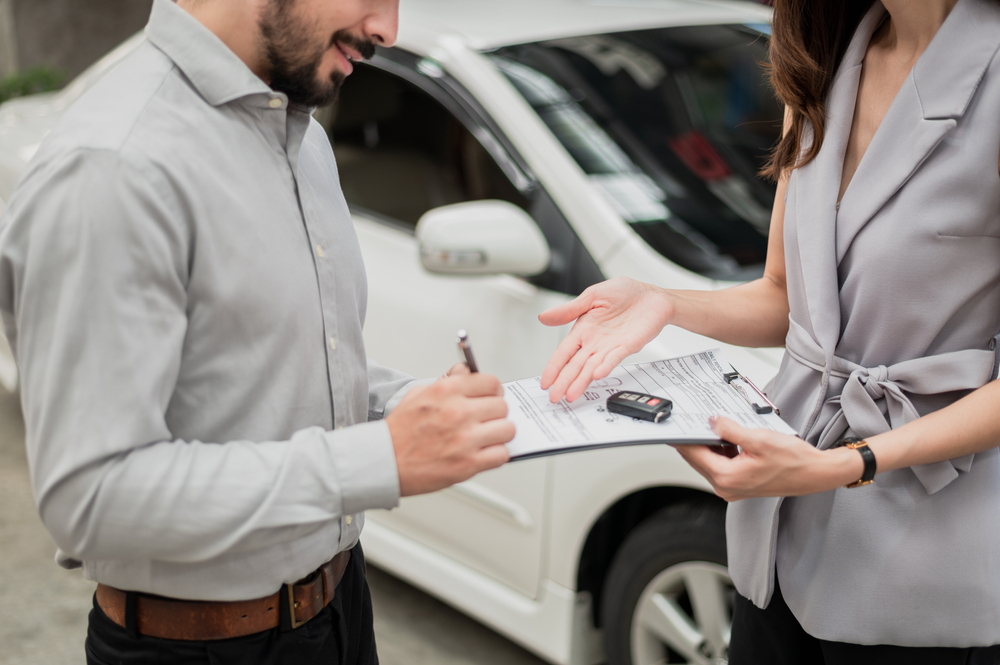 Automotive business, car insurance concept: Happy customer finalizing a deal and signing an insurance agreement with a car insurance agent.