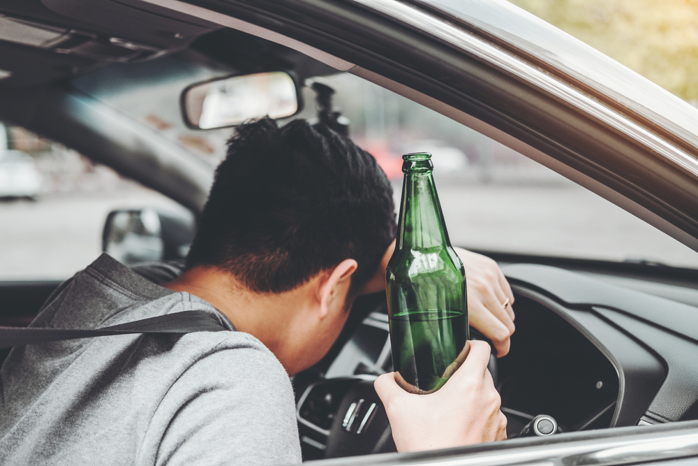 Drunk man driving a car on the road while holding a beer bottle. Dangerous drunk driving concept.